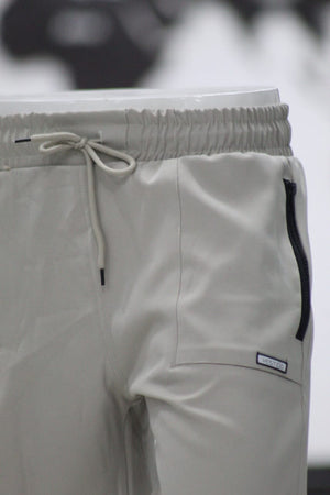 Close-up of light gray pants with a drawstring and brand label on a blurred background