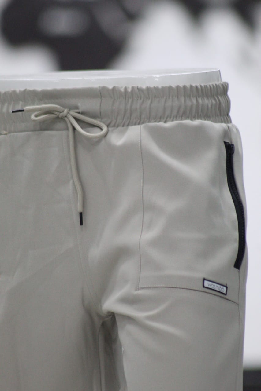 Close-up of light gray pants with a drawstring and brand label on a blurred background