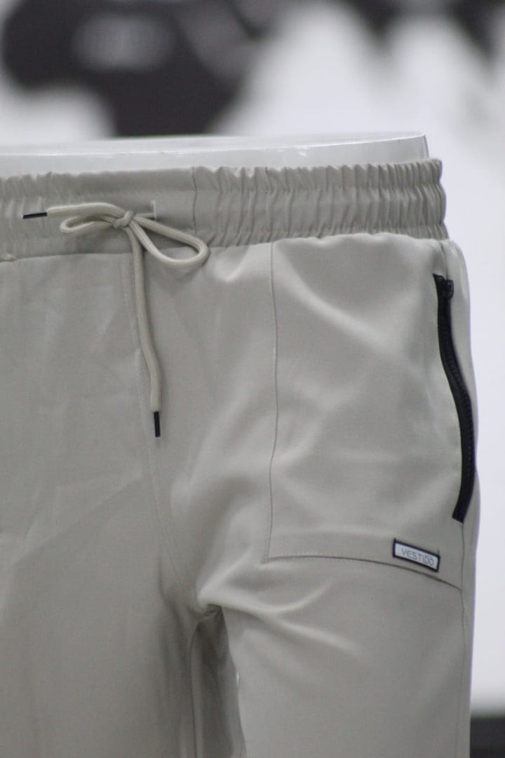 Close-up of light gray pants with a drawstring and brand label on a blurred background